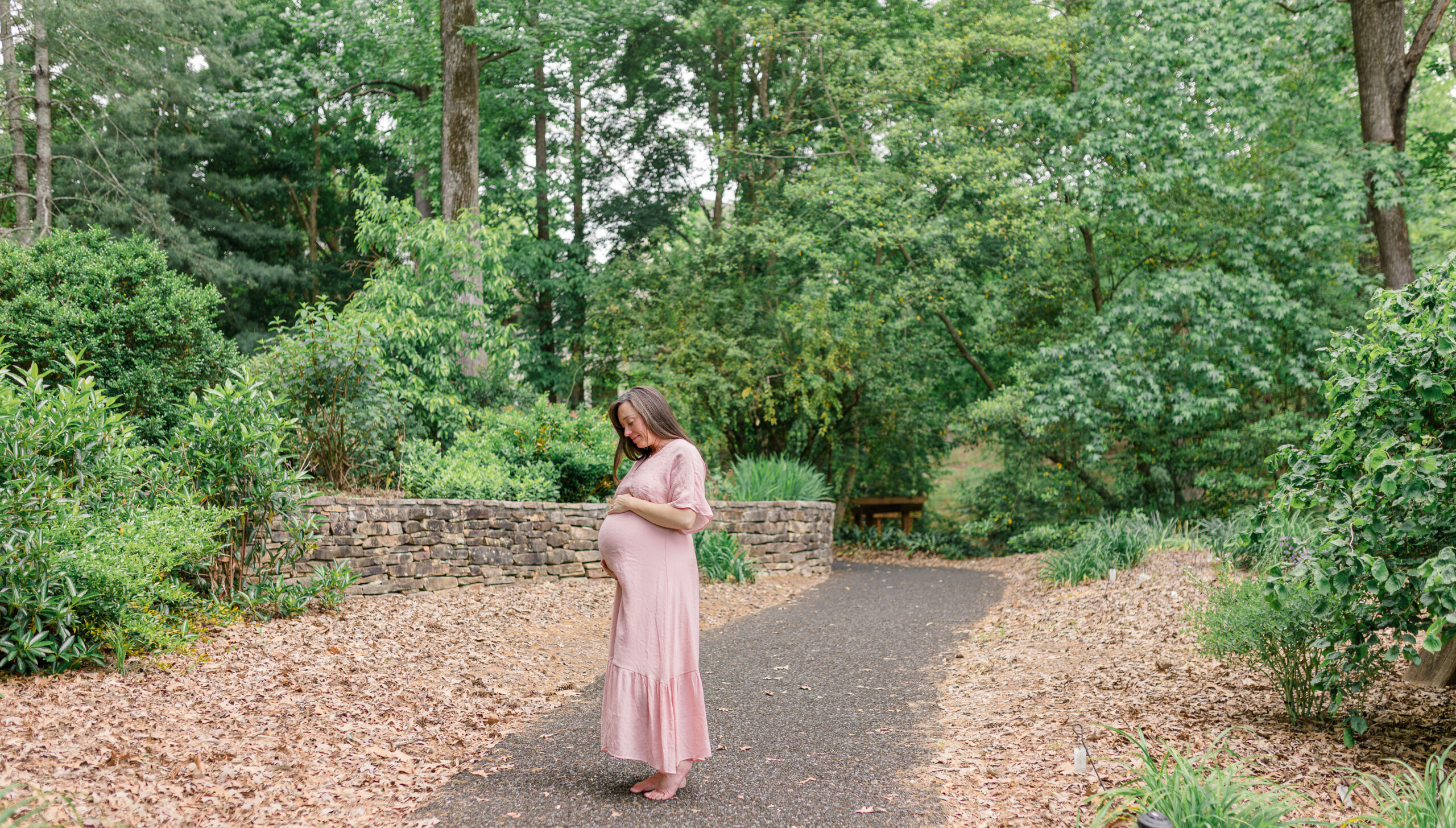 Jamie smiles as she holds her belly, surrounded by lush greenery during her spring maternity session.