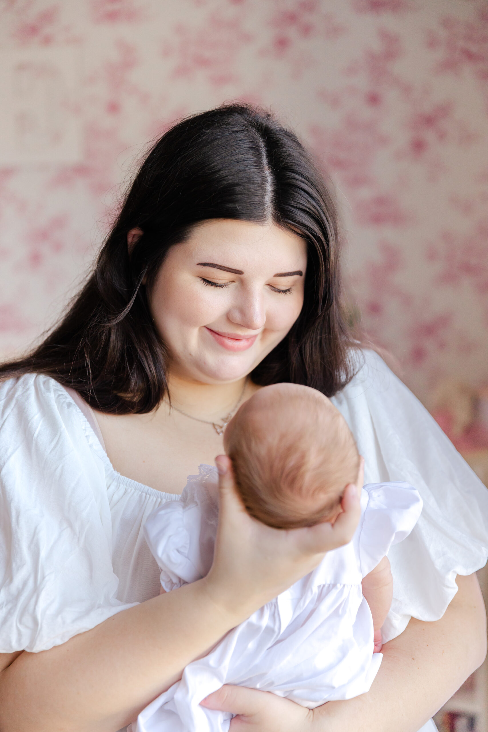 Mother holding her newborn baby, looking down at her lovingly with a soft smile.