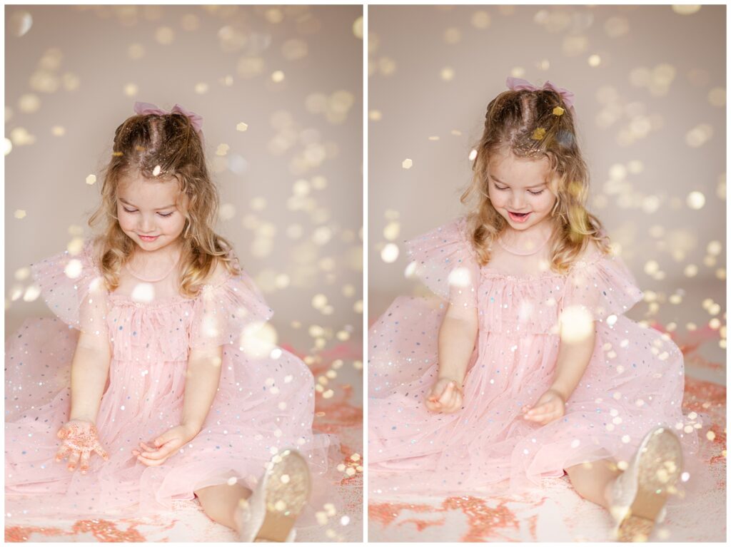 Little girl in a pink dress sitting down in glitter, looking down and smiling as she plays 