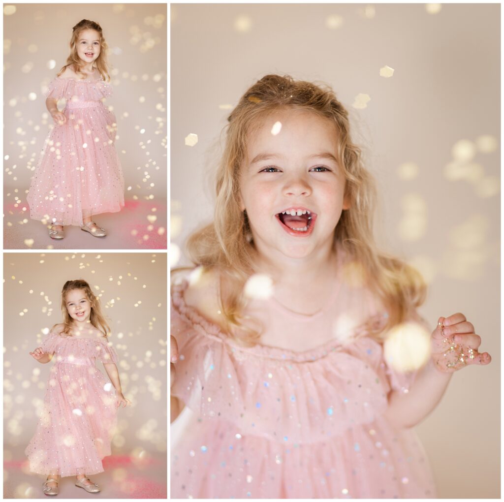 Little girl in a pink dress looking up and smiling as glitter falls down in a glitter photoshoot