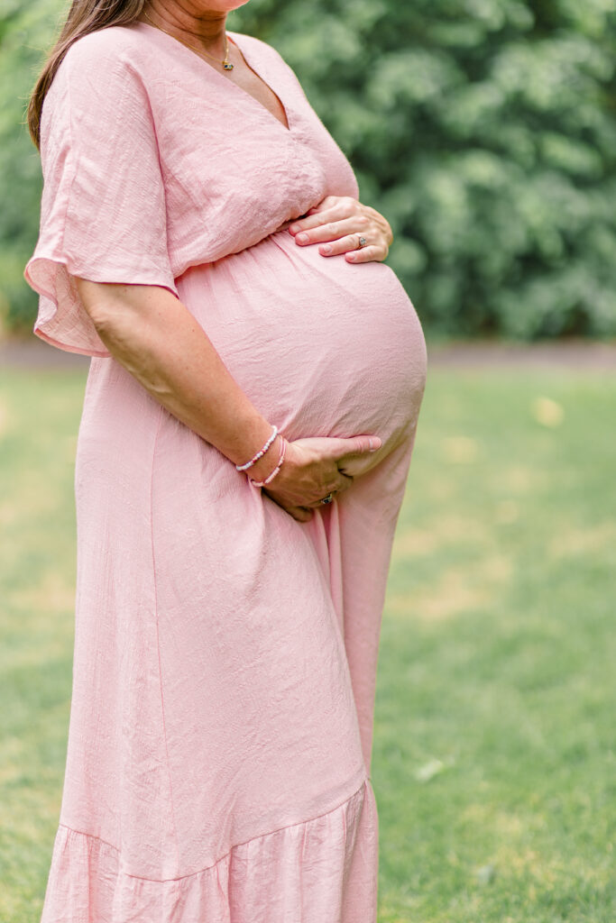 Woman in a pink dress cradling her pregnant belly