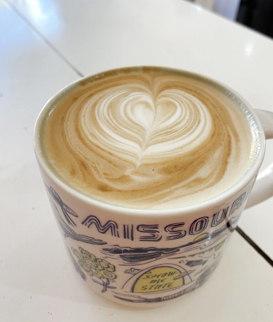 A latte in mug sitting on the table with a heart shaped design in the frothy milk.