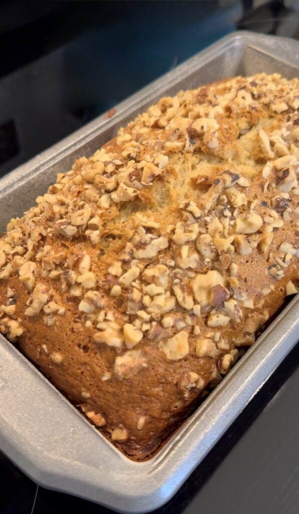 A loaf of golden brown banana walnut bread cooling on the stove.