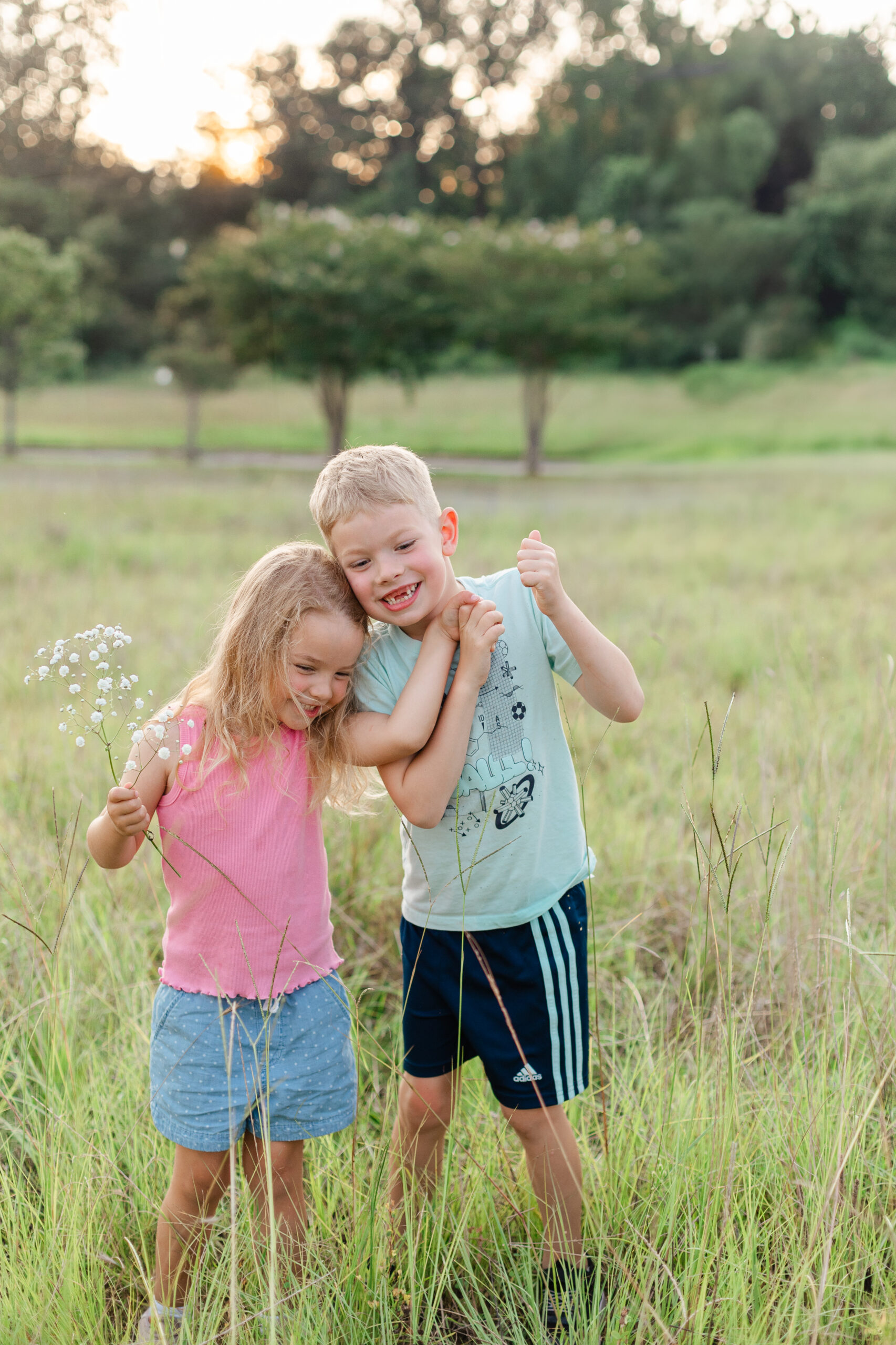 A little boy and girl who are brother and sister walking in a field, holding hands, and laughing.