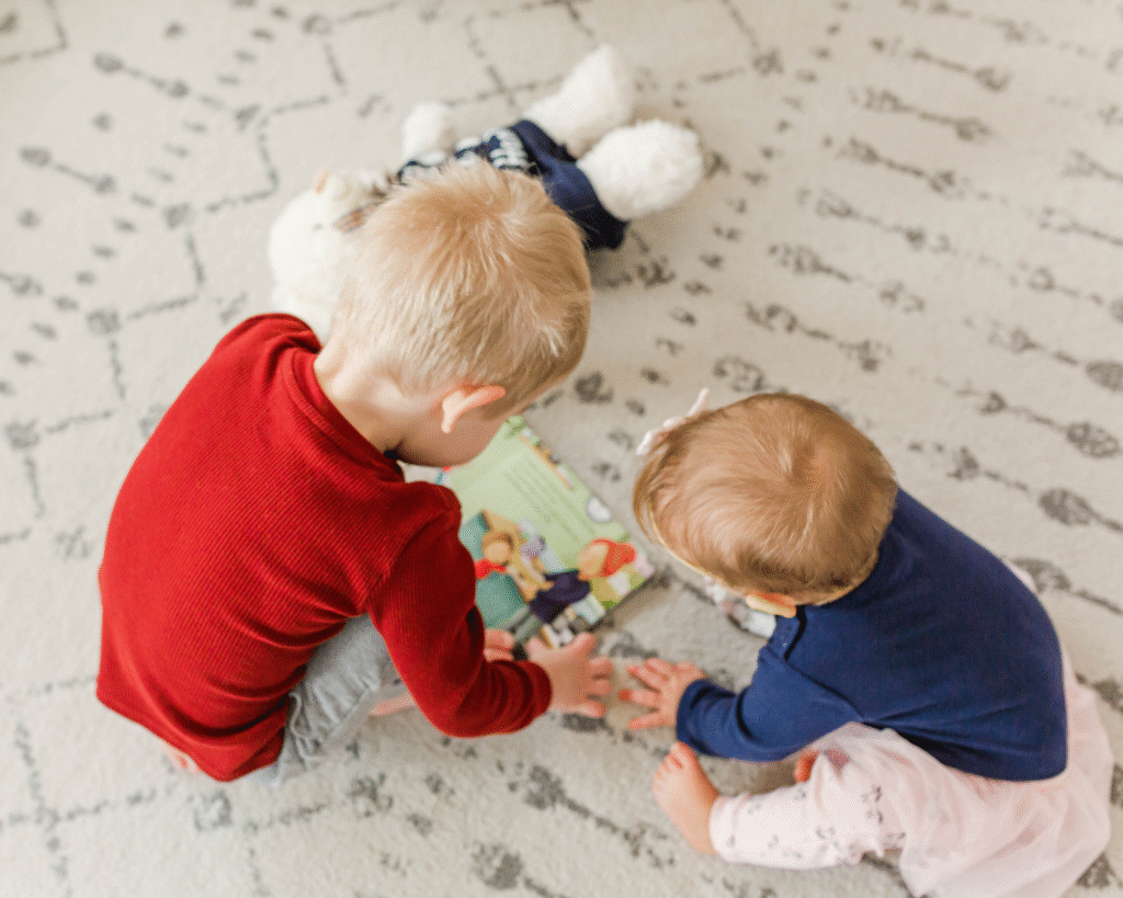 Older toddler brother reading a story to his baby sister