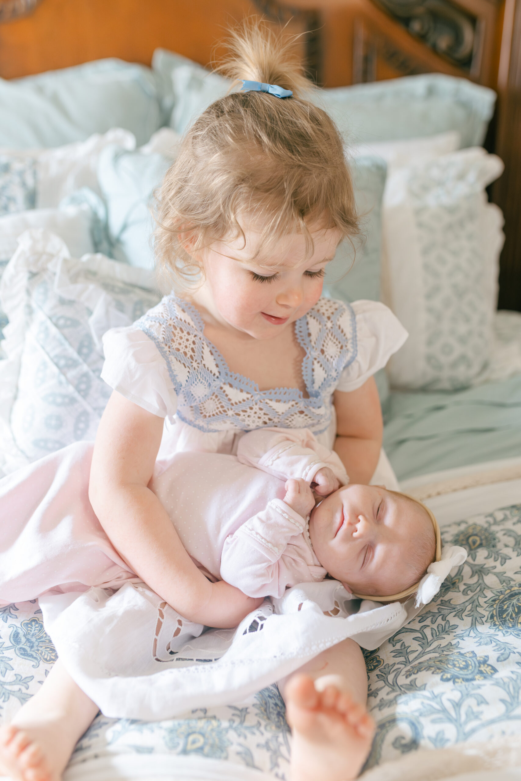 Older toddler sister holding her newborn sister