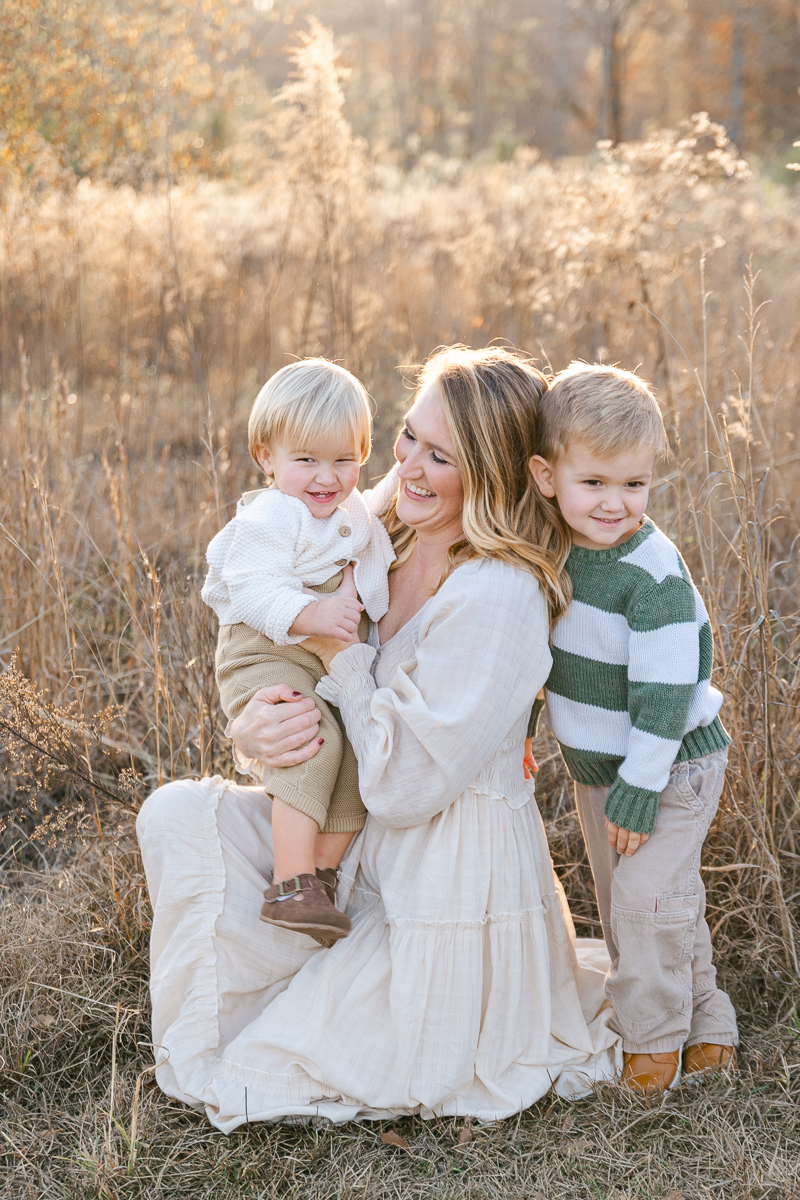 Mother sitting in a field at golden hour with her two sons, smiling at them