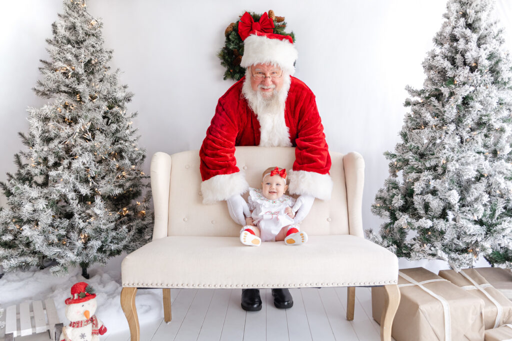 Baby seated on a bench with Santa close behind at a Tuscaloosa Santa mini session