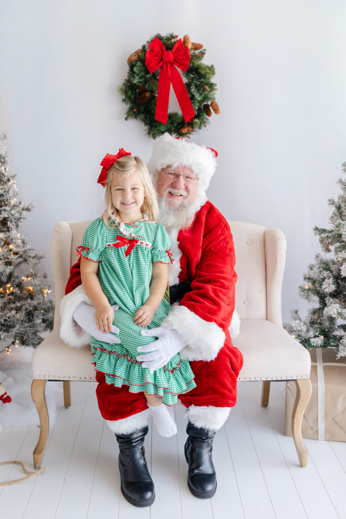 Little girl in a green dress smiling with Santa on a bench