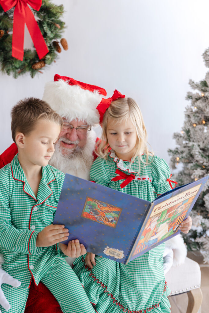 Santa reading a Christmas book with two children, keeping a gentle calm during a Santa mini session