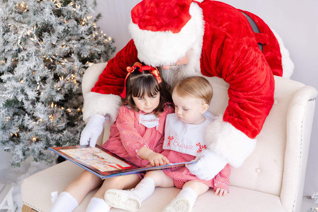 Siblings warming up together on a bench as Santa stays close during a Northport Christmas mini session