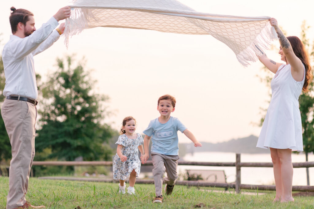 Two young children run beneath a blanket held up by their parents at golden hour in Tuscaloosa, Alabama